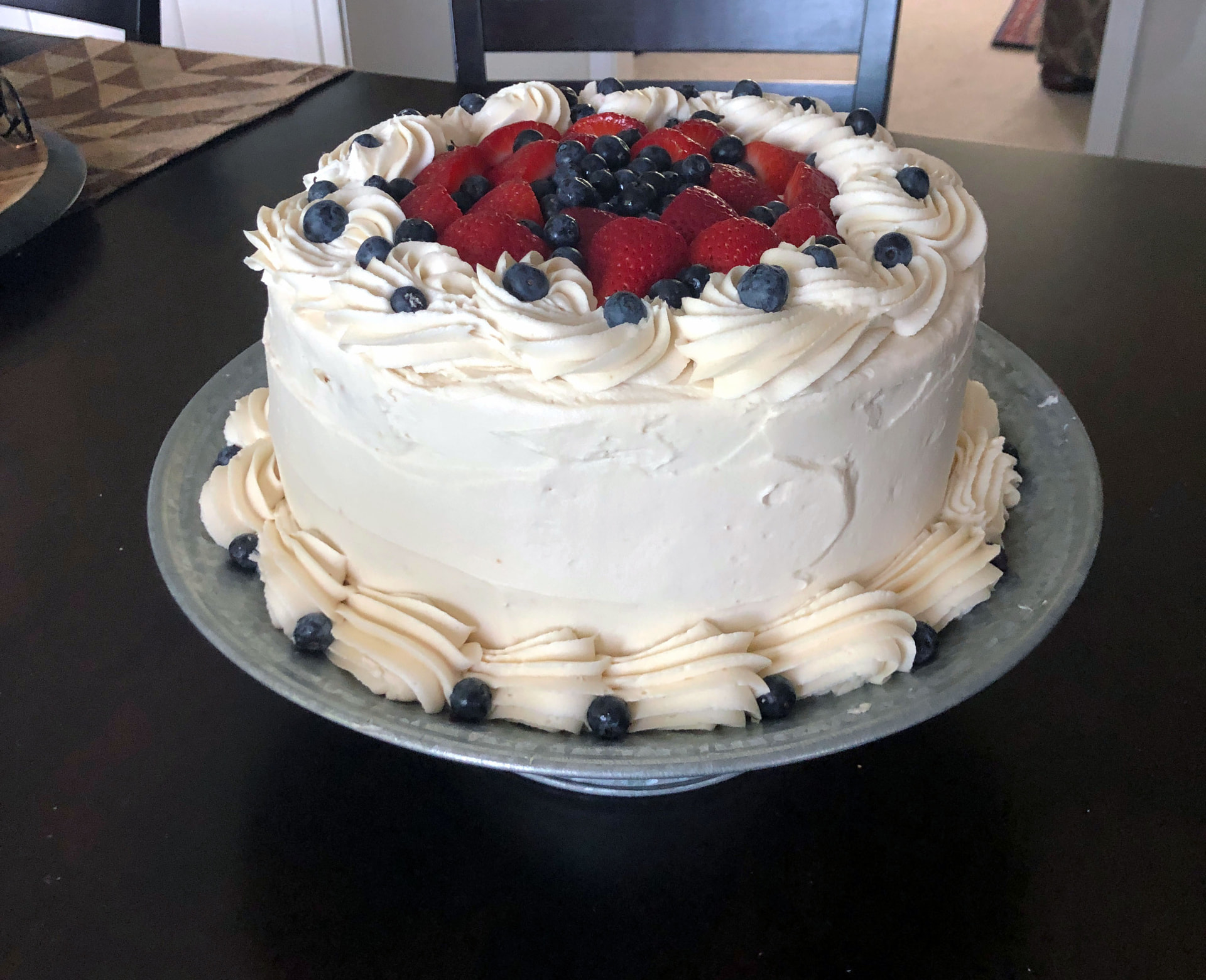 Layer cake with piped frosting rosettes topped with fresh strawberries and blueberries